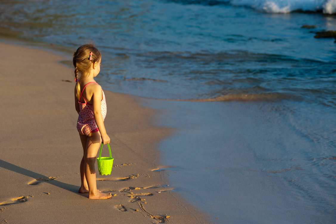 Niña con cubo mira el mar desde la orilla de la playa